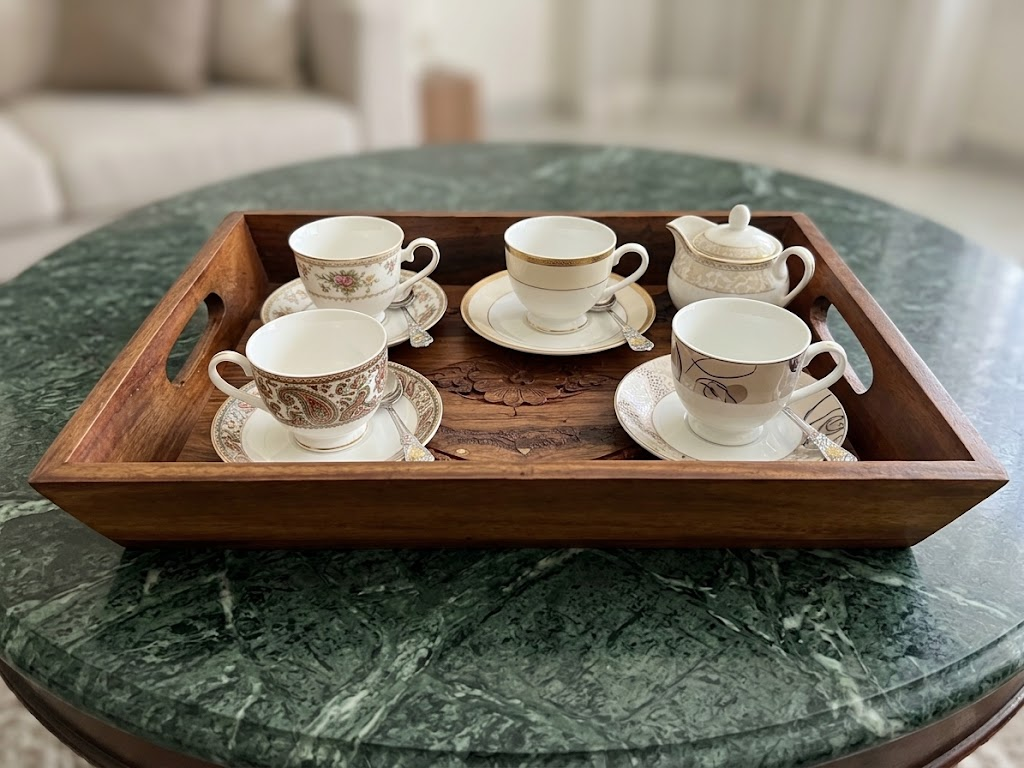 Wooden carved serving tray with tea cups and saucers on green marble table