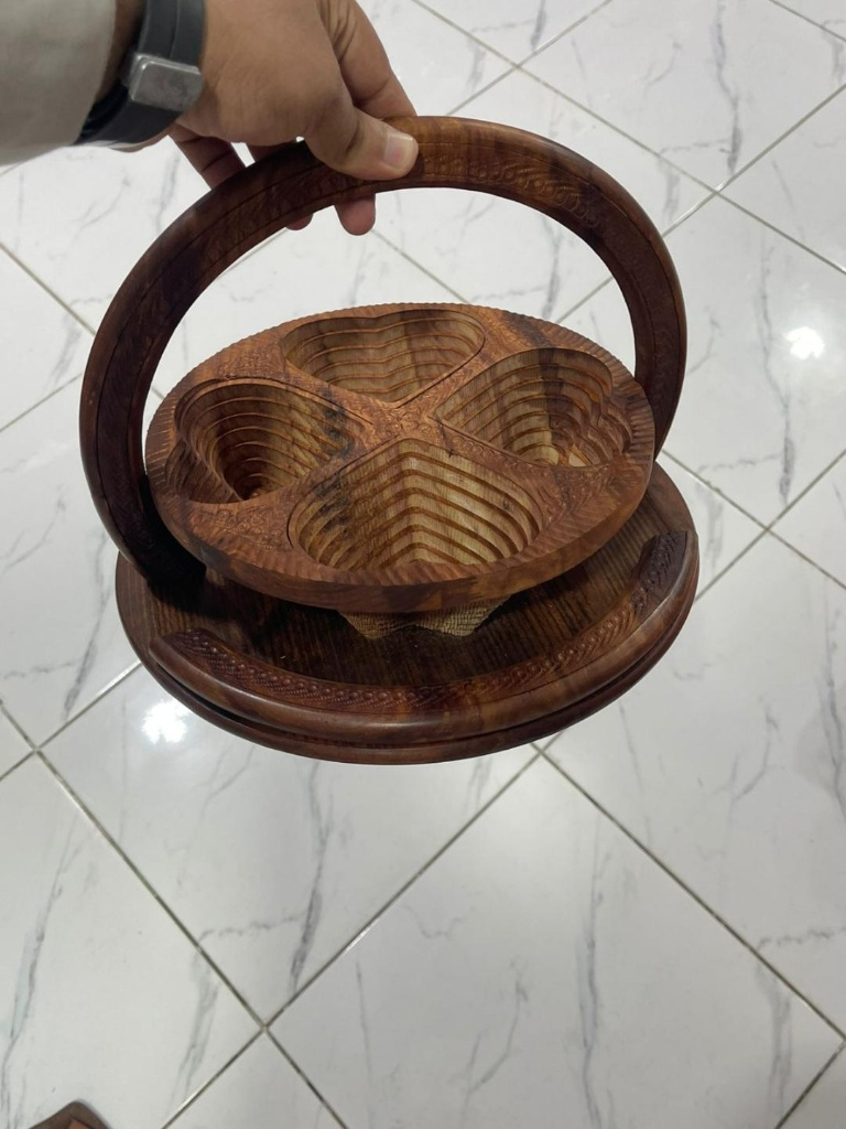 Hand holding wooden dry fruit tray showing carved interior compartments